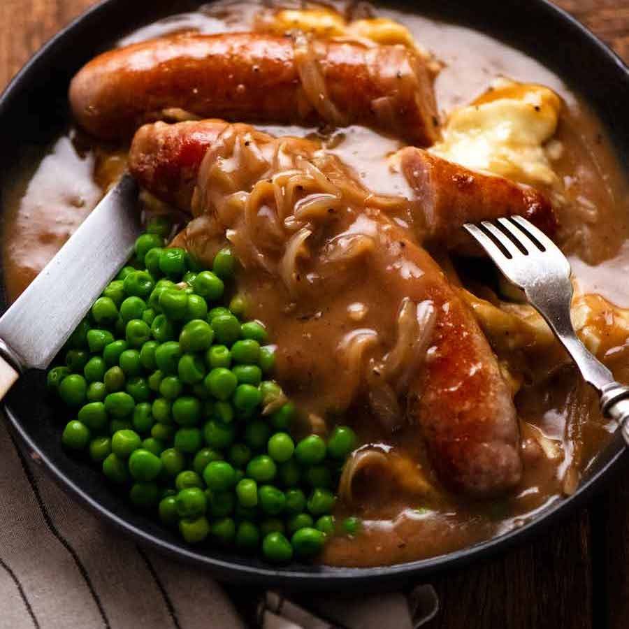 Bangers and Mash (Sausage with Onion Gravy) on a plate with mashed potato and peas