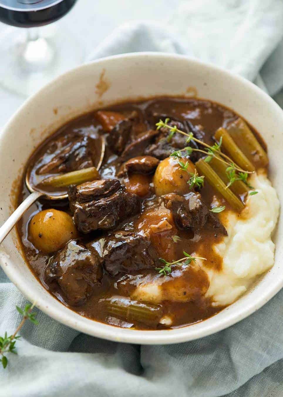 Photo of Beef Stew over mashed potato in a rustic cream bowl.