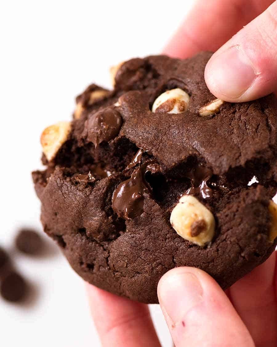 Close up of hand breaking a Better than Byron Bay Triple Chocolate Cookie. Chewy on the inside, 40% chocolate, with crispy edges.